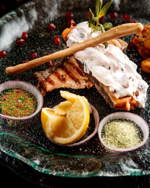 Side view of baked fish fillet  garnished with vegetables   spices and sauce on a plate