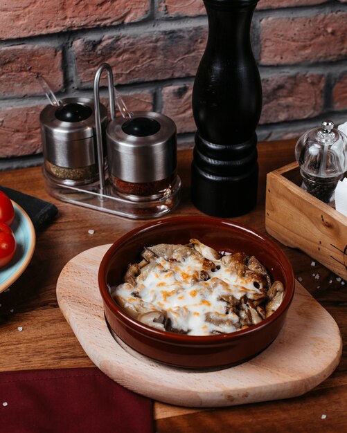 Side view of baked mushroom with cheese in a clay bowl