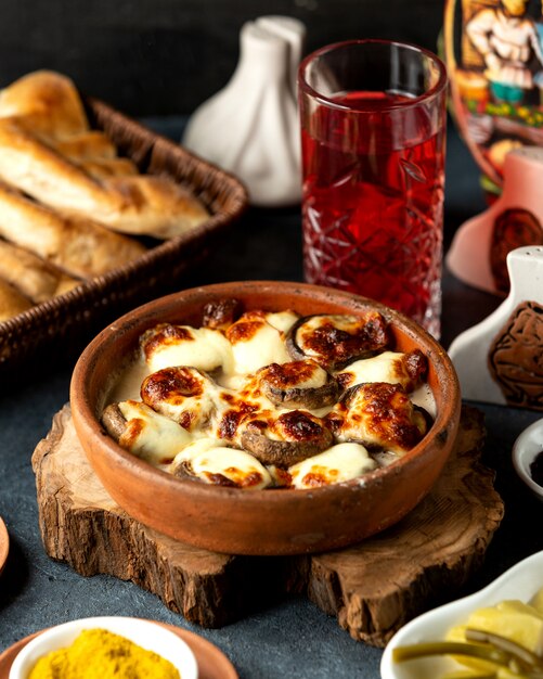 Side view of baked mushrooms with cheese in a clay bowl