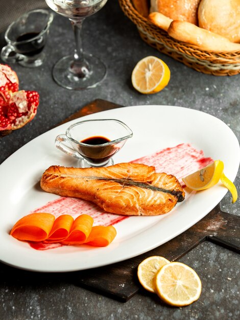 Side view of baked salmon served with narsharab pomegranate sauce and lemon on white plate