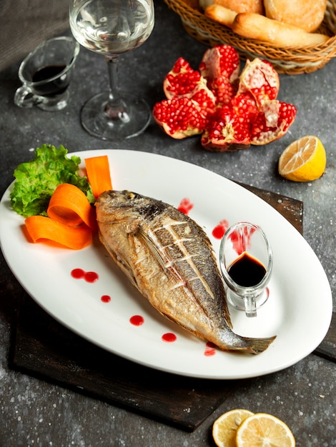 Free photo side view of baked sea bass served with lemonnd narsharab sauce on white platter on black
