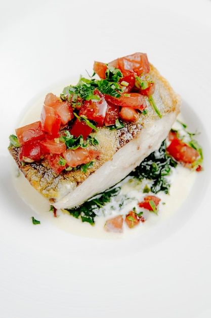 Side view of baked seabass with tomatoes on white surface