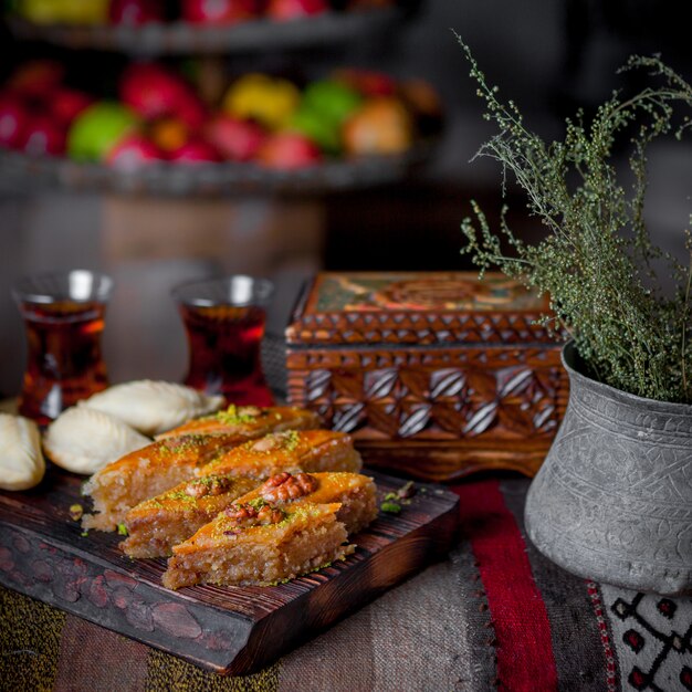 Side view baklava with shekerbura and casket and glass of tea in wooden plank