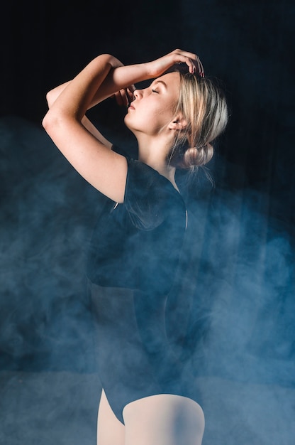 Side view of ballerina posing with arms in smoke