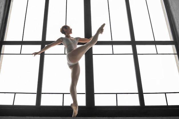 Free photo side view of ballerina stretching by the window