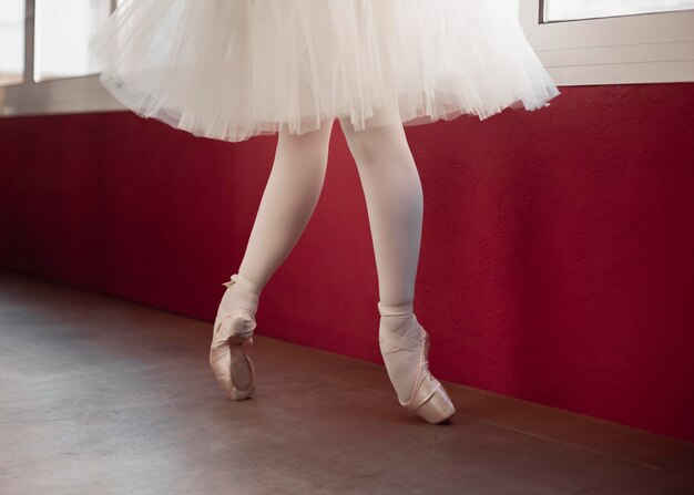 Балерина в юбке-пачке тренируется рядом с окном, вид сбоку