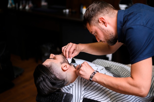 Side view barber cutting client's beard