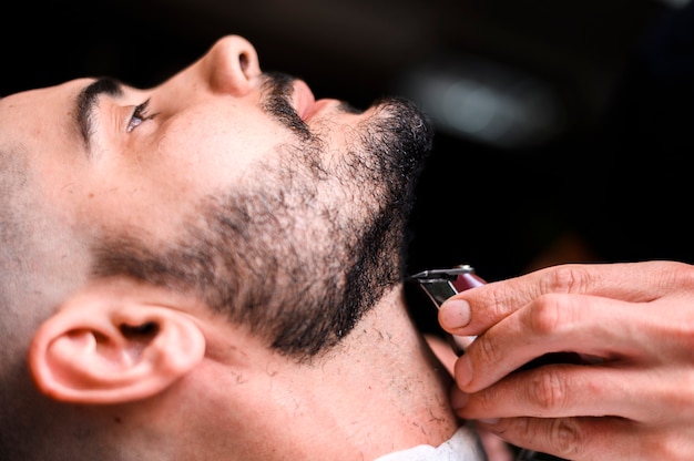 Side view barber shaving client's beard close-up