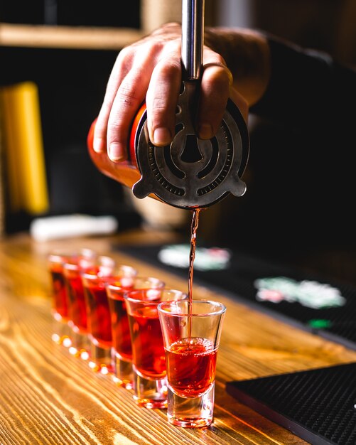 Side view bartender pours into shots a drink from a shaker