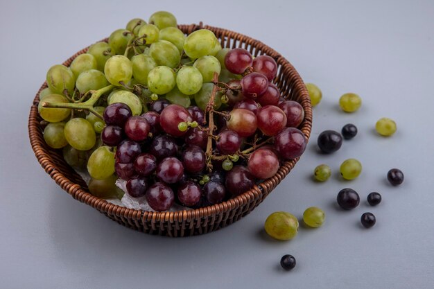 Side view of basket of grapes and grape berries on gray background