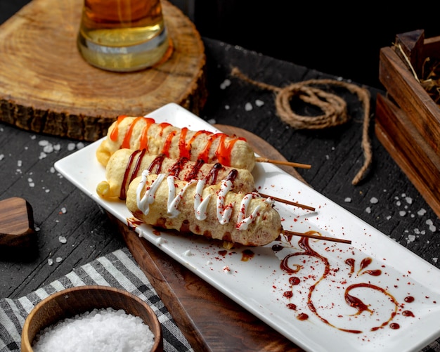 Side view of battered sausage on wooden sticks with sauce on a plate