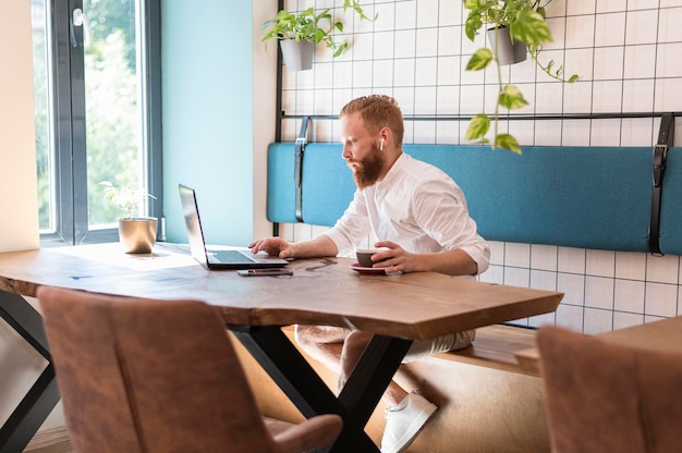 Side view bearded man holding a cup of coffee while working