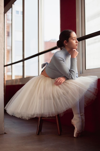 Side view of beautiful ballerina in tutu skirt posing next to window