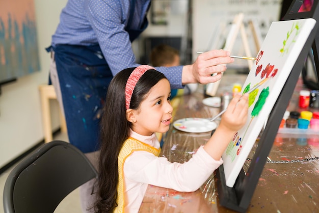 子供のための彼女のアートクラスの間にキャンバスにかわいい絵を描いている美しい小学生の側面図