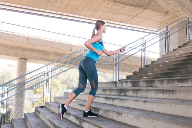 Free photo side view of a beautiful female athlete running on staircase