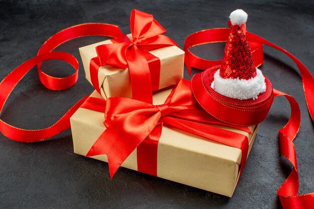 Side view of beautiful gifts with red ribbon and santa claus hat on dark background