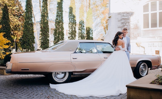 화창한 날 분홍색 차 배경에 서 있는 아름다운 신혼부부의 모습