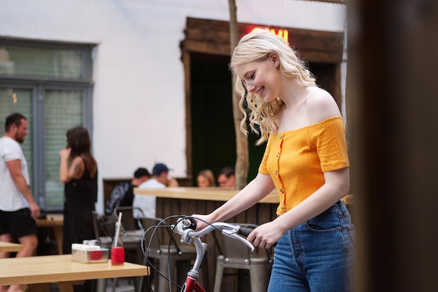 Side view of beautiful smiling blond girl happily standing with classic bicycle in courtyard of city cafe