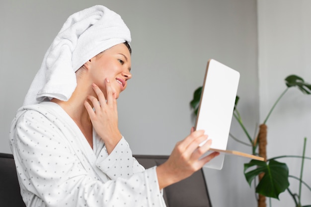 Free photo side view of beautiful woman looking in the mirror while indulging in self care