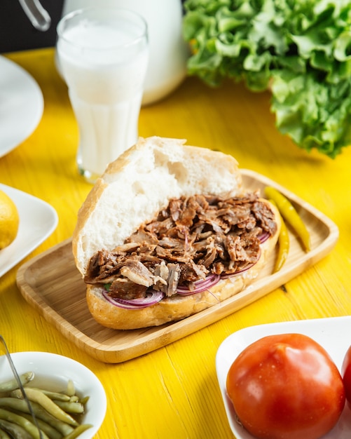 Side view of beef doner in bread with pickled green pepper on wooden platter