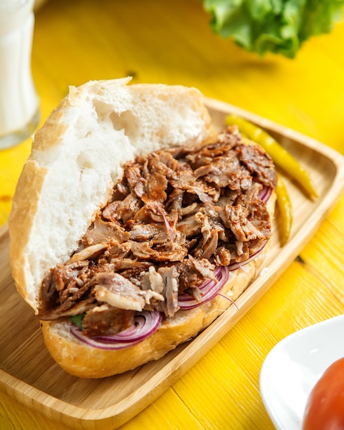Side view of beef doner in bread with pickled green pepper on wooden platter