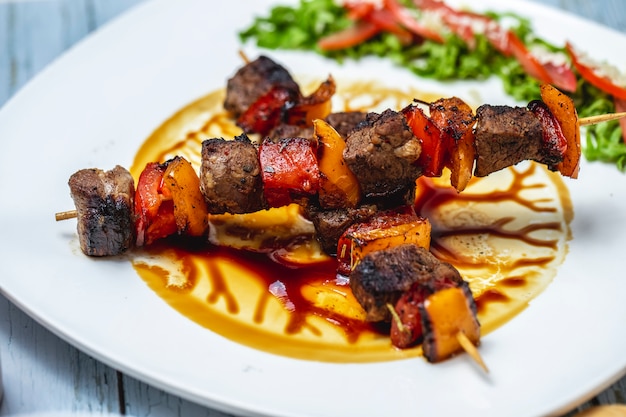 Side view beef kebabs grilled beef with tomato red and yellow peppers and sauce on a plate