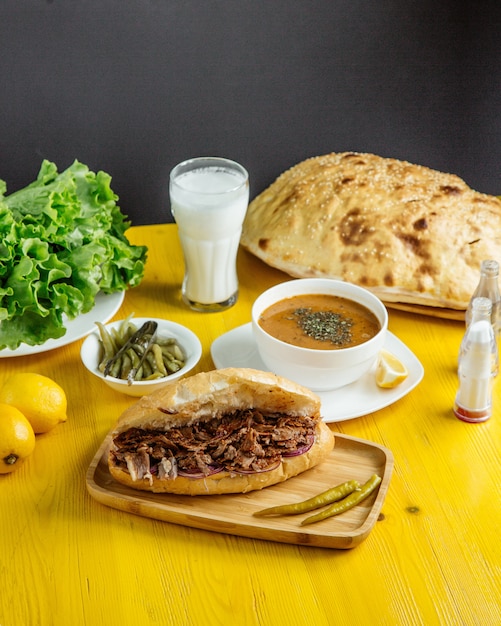 Side view of beef meat doner in bread served with pckles and soup on the table