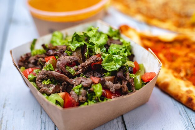 Side view beef salad sliced red meat with tomato bell pepper and lettuce in box
