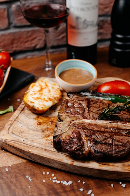 Side view of beef steak served with baked vegetables and barbeque sauce on wooden board