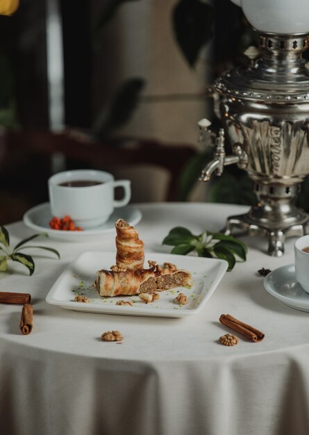 Side view of biscuit roll filled with walnuts served with tea on a table