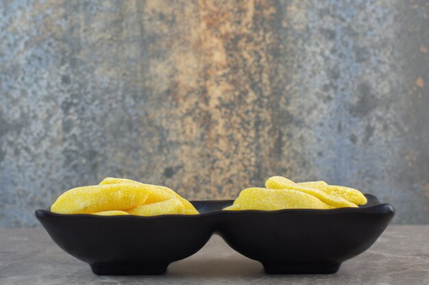 Side view of black bowl full with yellow sweet candies.