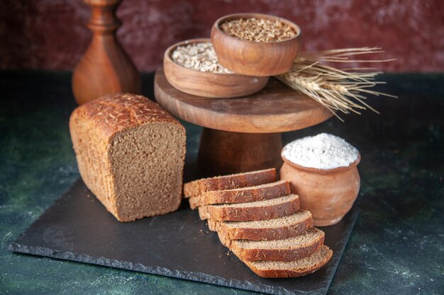 黒のトレイに黒パンのスライスと栗色の背景に茶色のボウルに小麦粉の側面図