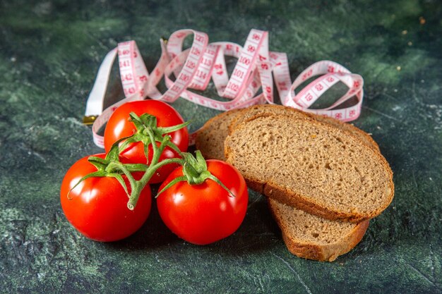 Side view of black bread slices fresh tomatoes with stem and meters on dark colors surface