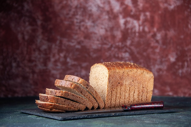 Side view of black bread slices knife on dark color board on mixed colors distressed background