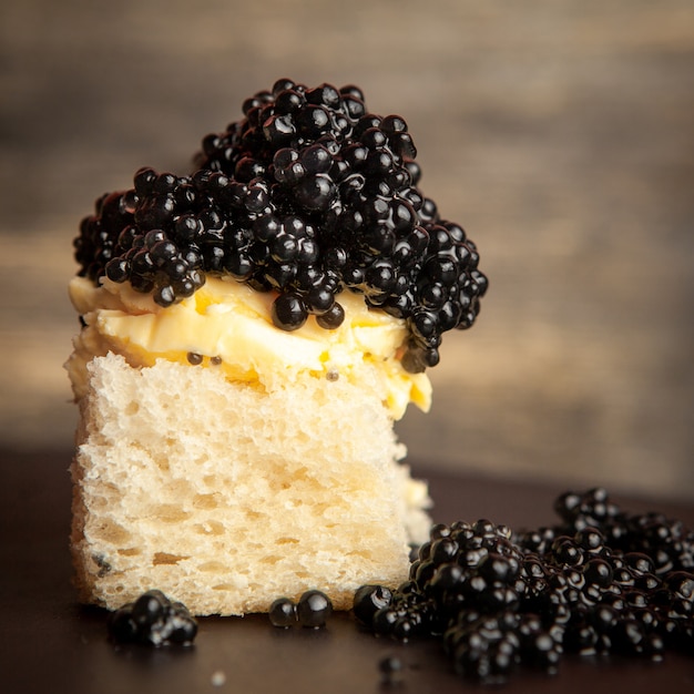 Side view black caviar with butter on bread on dark background.