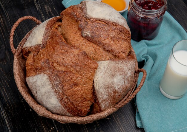 Side view of black cob in basket with butter jam milk on cloth and wooden surface