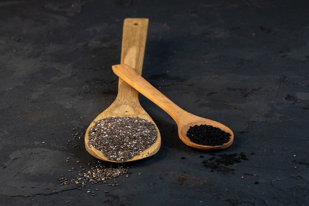 Side view of black cumin seeds in wooden spoons on black