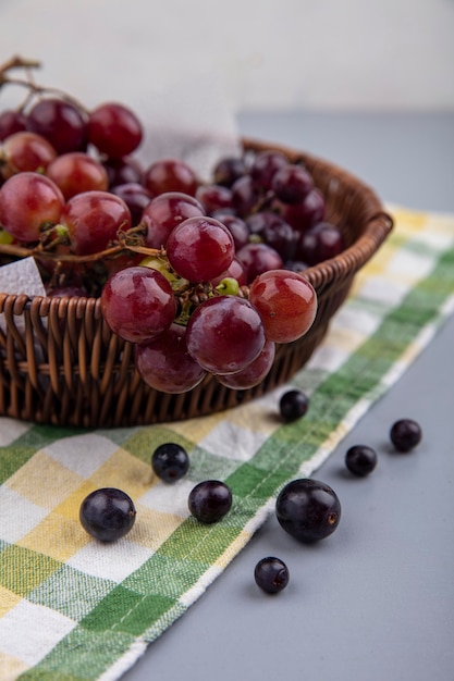 Side view of black grape in basket on plaid cloth on gray background