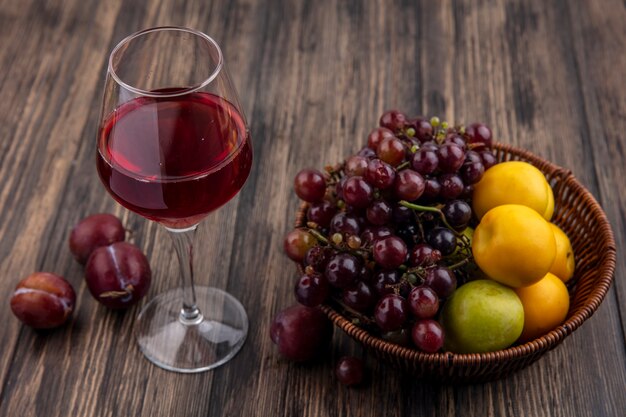 나무 배경에 바구니에 포도 pluot nectacot으로 과일과 함께 와인 글라스에 검은 포도 주스의 측면보기