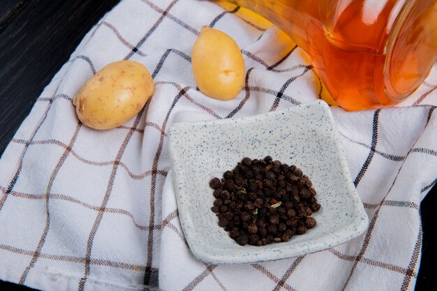 Side view of black pepper seeds and potatoes with melted butter on plaid cloth and wooden table