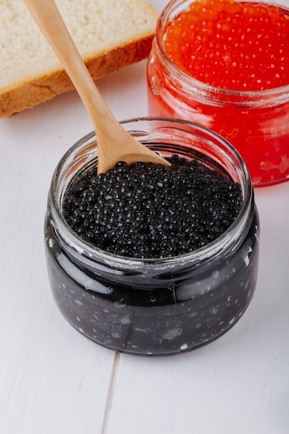 Side view black and red caviar in glass jars with a spoon