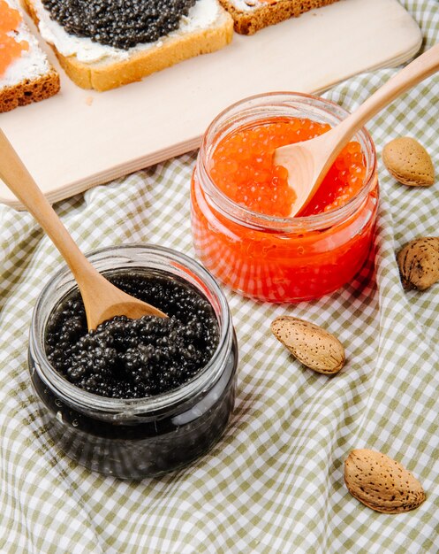 Free photo side view black and red caviar jar with wooden spoon and almond on the table