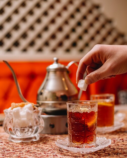 Вид сбоку черный чай с ломтиком лимона и чайником на столе