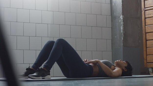 Вид сбоку на чернокожую женщину, занимающуюся тренировкой пресса на полу в синем лофте.