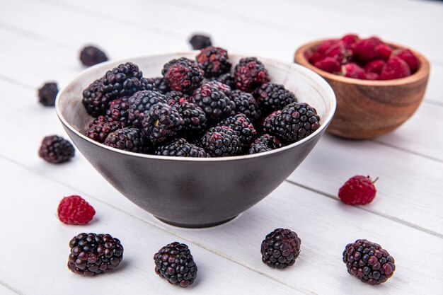 Side view of blackberry in a bowl with raspberries on a white surface