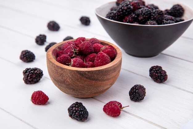 Side view of blackberry in a bowl with raspberries on a white surface