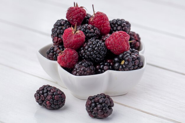 Side view of blackberry with raspberries in a bowl on a white surface