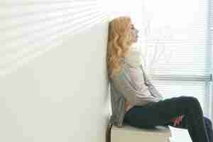 Free photo side view of blond woman sitting exhausted and pondering in a room