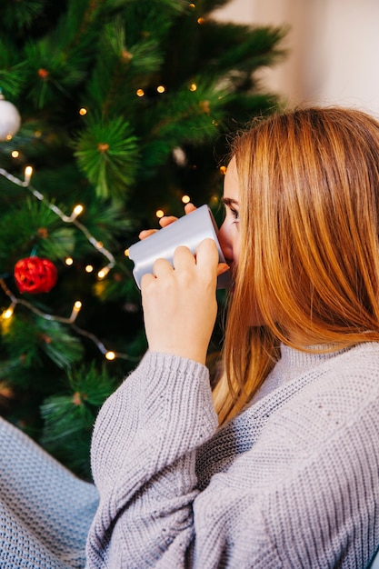 クリスマスツリーの前でお茶を飲むブロンドの女性の側面図