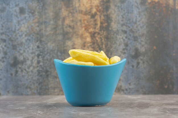 노란색 달콤한 사탕으로 가득 찬 파란색 세라믹 그릇의 측면 보기.